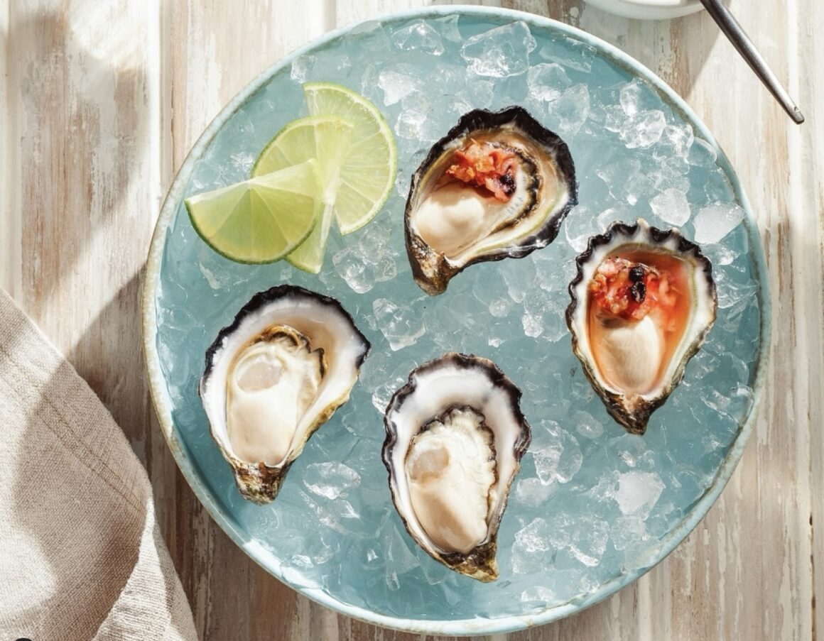 A bowl of ice with four oysters sitting a top it with lime slices 